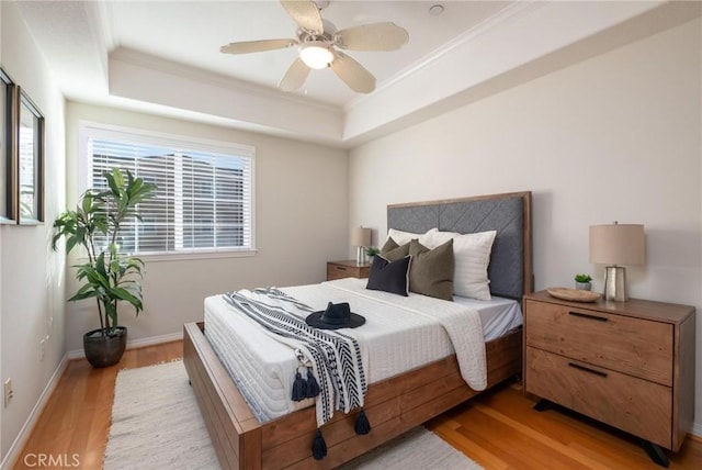 bedroom featuring crown molding, a raised ceiling, ceiling fan, and light wood-type flooring