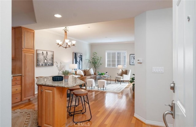 kitchen with pendant lighting, crown molding, a kitchen breakfast bar, light stone counters, and light wood-type flooring