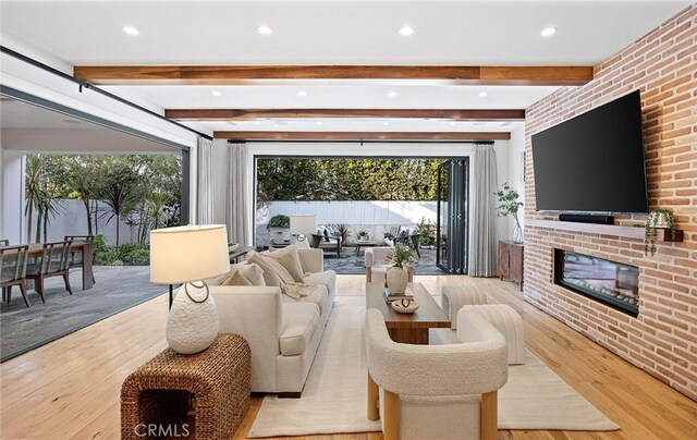 living room featuring a brick fireplace, beam ceiling, and light hardwood / wood-style flooring