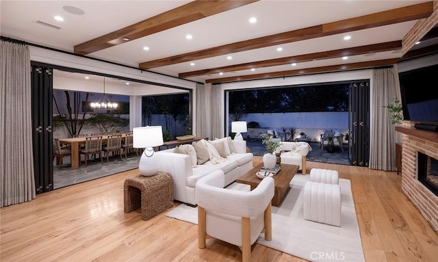 home theater room featuring beam ceiling, visible vents, a brick fireplace, wood finished floors, and a chandelier