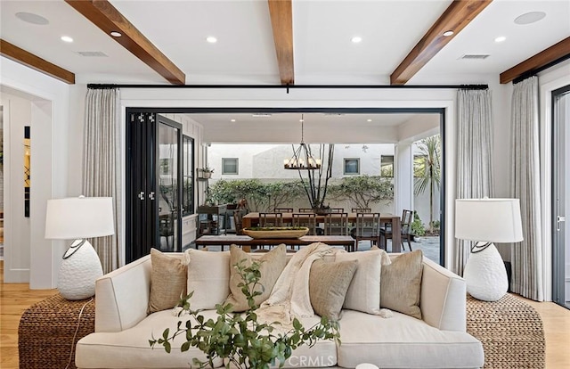 living room featuring light wood-style flooring, visible vents, a chandelier, and beamed ceiling