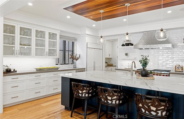 bar with decorative light fixtures, white cabinetry, custom exhaust hood, paneled built in refrigerator, and light stone counters