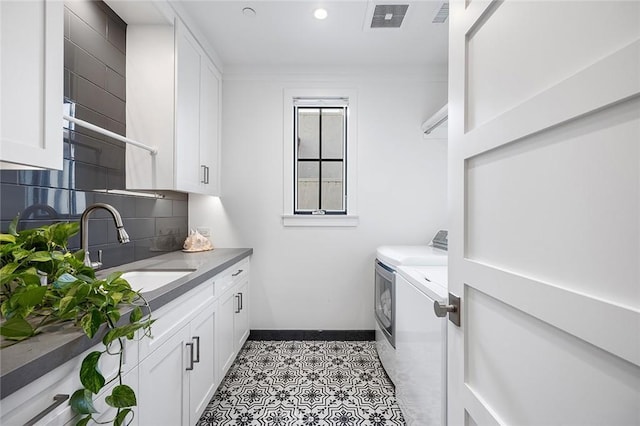 washroom with a sink, visible vents, baseboards, washer and dryer, and cabinet space