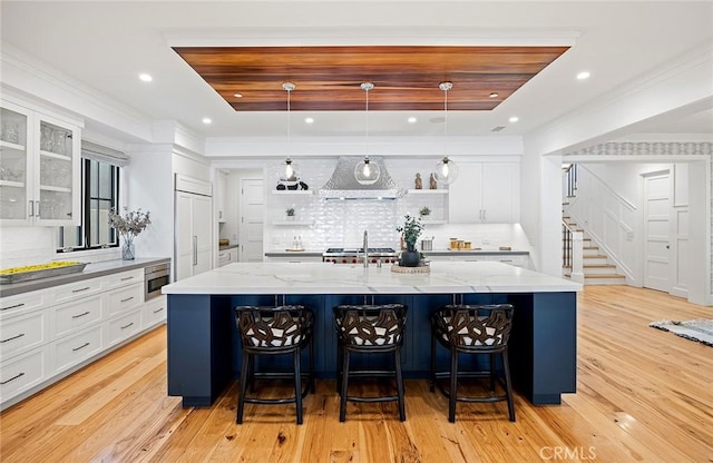 kitchen featuring extractor fan, built in appliances, a large island with sink, pendant lighting, and white cabinets