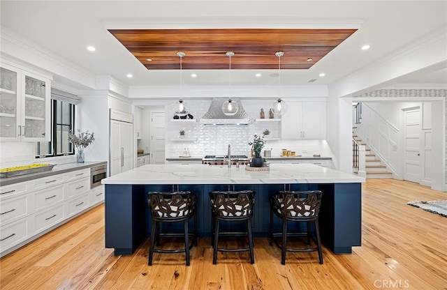 kitchen featuring built in appliances, white cabinetry, range hood, open shelves, and a large island with sink