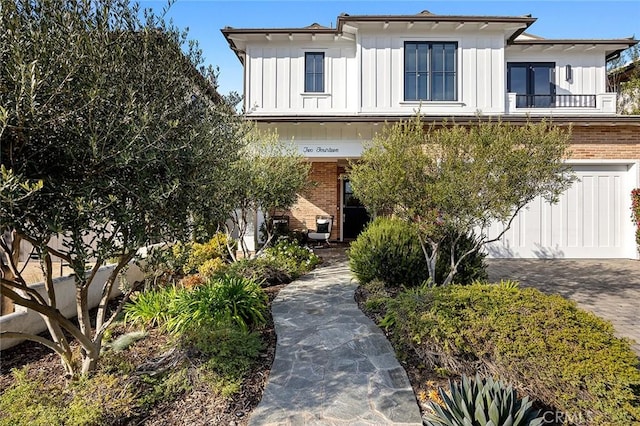 view of front of house with a balcony, decorative driveway, board and batten siding, and brick siding