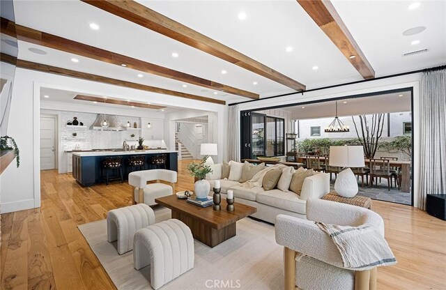 living room featuring beamed ceiling, a wealth of natural light, a notable chandelier, and light hardwood / wood-style floors