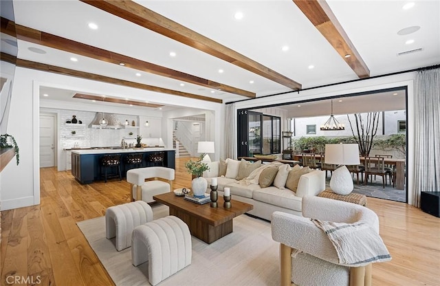 living area featuring a chandelier, visible vents, light wood-style floors, stairway, and beamed ceiling