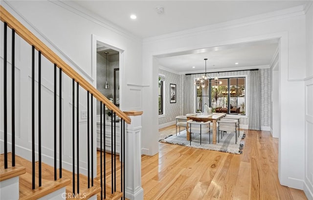 entryway with wallpapered walls, ornamental molding, wood finished floors, stairs, and a chandelier