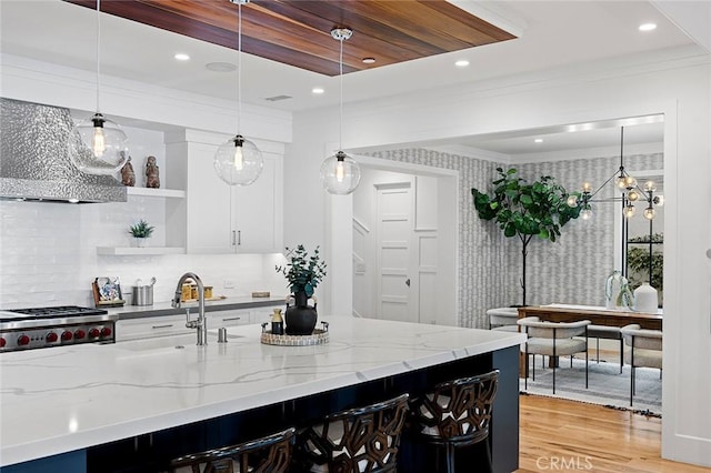 kitchen with sink, extractor fan, white cabinetry, decorative light fixtures, and light stone countertops