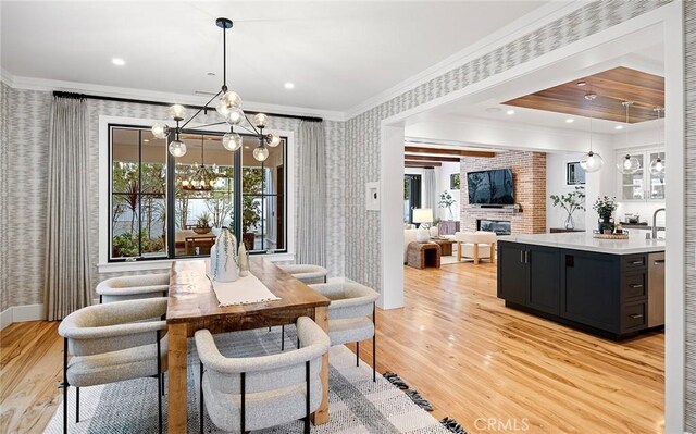 dining room featuring an inviting chandelier, ornamental molding, a fireplace, and light hardwood / wood-style floors