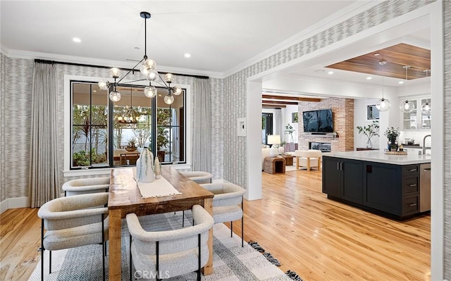 dining space with a chandelier, light wood-style flooring, a fireplace, wallpapered walls, and crown molding