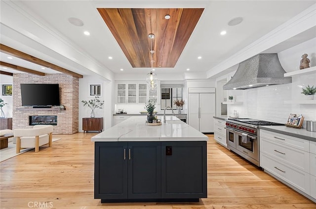 kitchen featuring pendant lighting, white cabinets, premium appliances, a center island with sink, and wall chimney exhaust hood