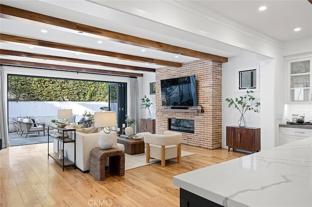 living room featuring crown molding, beam ceiling, a brick fireplace, and light hardwood / wood-style flooring