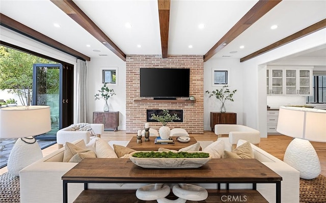 living room with recessed lighting, beamed ceiling, a brick fireplace, and light wood-style floors