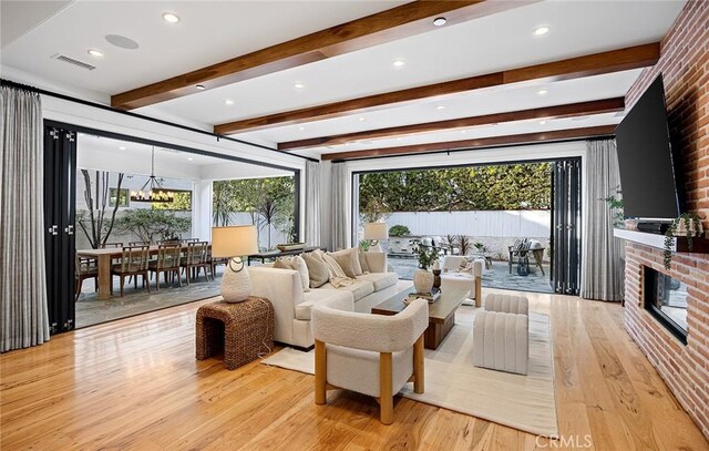 living room with an inviting chandelier, a brick fireplace, light hardwood / wood-style flooring, and a wealth of natural light