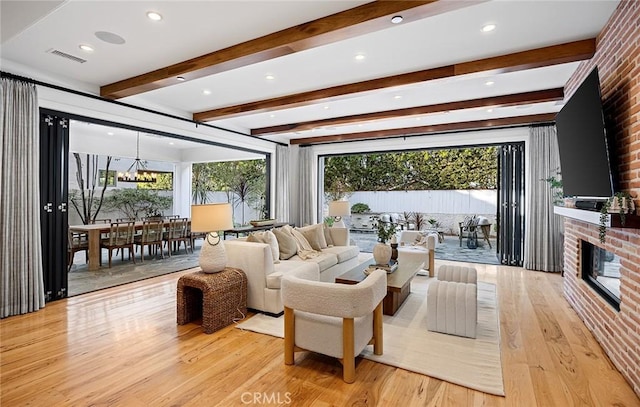 living room featuring light wood finished floors, a healthy amount of sunlight, a brick fireplace, and an inviting chandelier