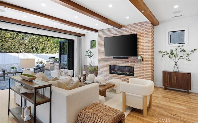 living room with a fireplace, beam ceiling, and light wood-type flooring