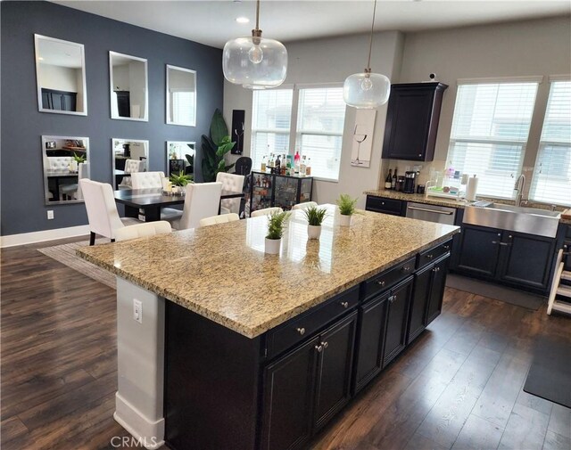 kitchen featuring sink, light stone counters, a center island, hanging light fixtures, and dark hardwood / wood-style flooring