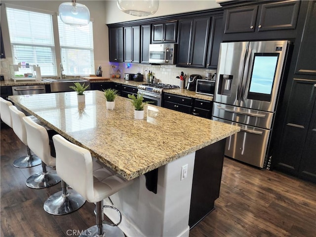 kitchen featuring a breakfast bar area, appliances with stainless steel finishes, hanging light fixtures, backsplash, and a kitchen island