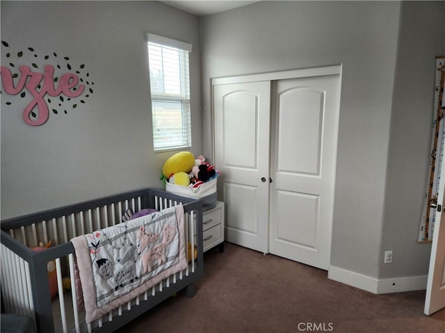 bedroom featuring a nursery area, a closet, and dark colored carpet