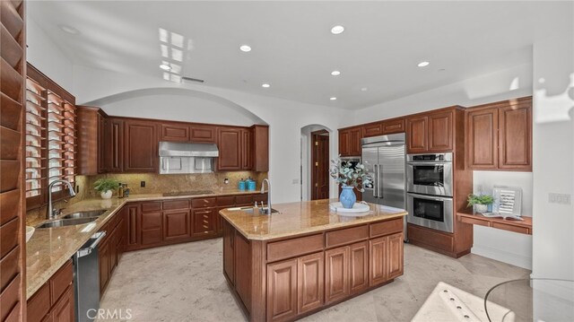 kitchen featuring sink, backsplash, stainless steel appliances, and a center island with sink