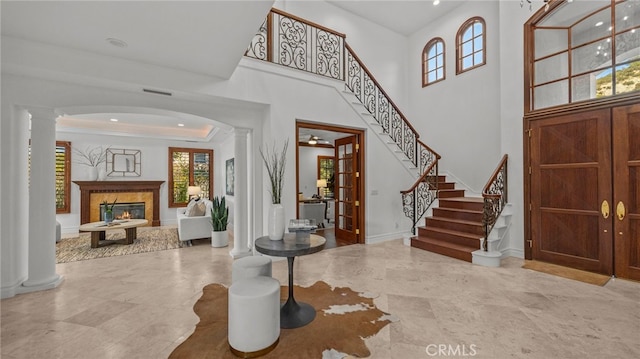 foyer entrance featuring a towering ceiling, a fireplace, and ornate columns