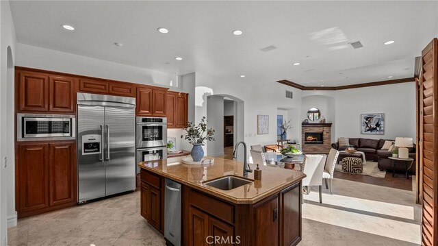 kitchen featuring sink, appliances with stainless steel finishes, ornamental molding, an island with sink, and a fireplace