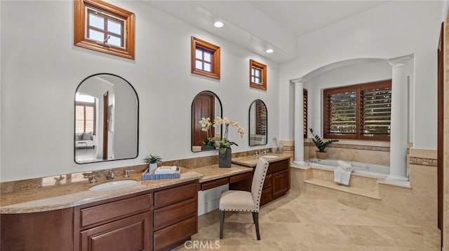 bathroom featuring vanity, a relaxing tiled tub, and decorative columns