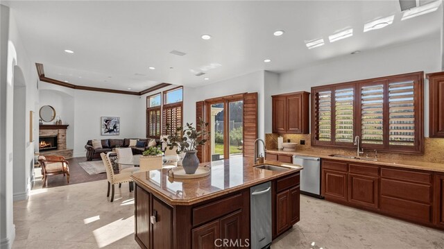 kitchen with sink, a kitchen island with sink, stainless steel dishwasher, and a stone fireplace