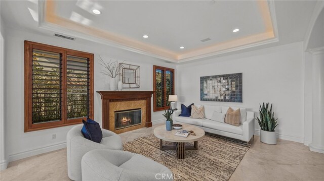 living room featuring a premium fireplace, ornamental molding, and a raised ceiling