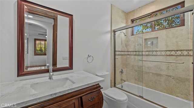 full bathroom with bath / shower combo with glass door, vanity, and toilet