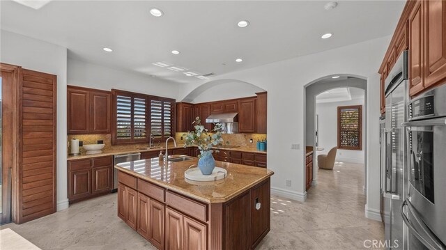 kitchen featuring light stone countertops, sink, a center island with sink, and decorative backsplash