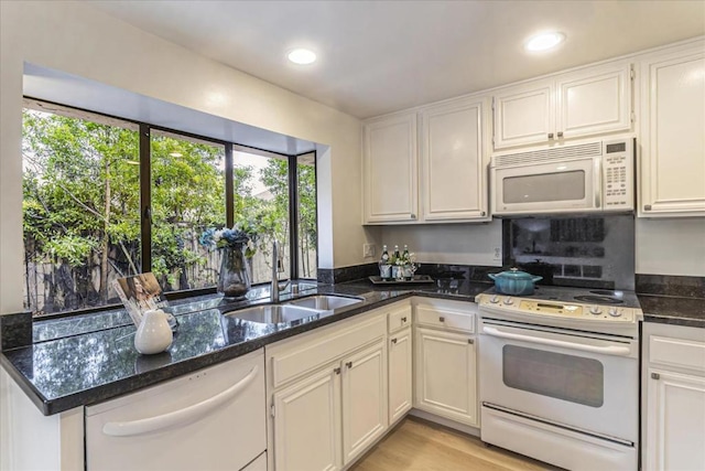 kitchen with sink, white appliances, dark stone countertops, light hardwood / wood-style floors, and white cabinets