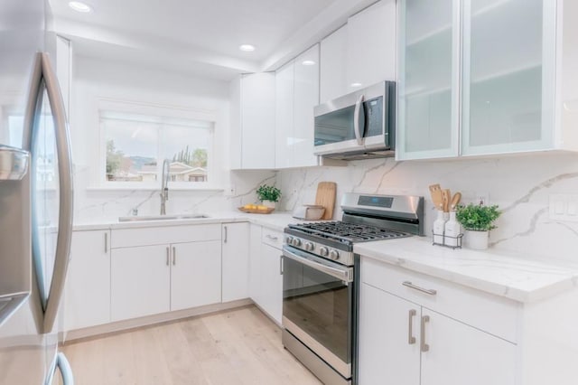 kitchen featuring sink, white cabinetry, light hardwood / wood-style flooring, appliances with stainless steel finishes, and decorative backsplash