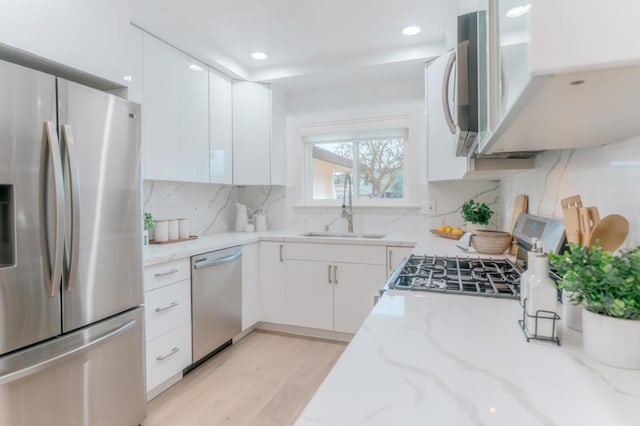 kitchen with sink, tasteful backsplash, stainless steel appliances, light stone countertops, and white cabinets