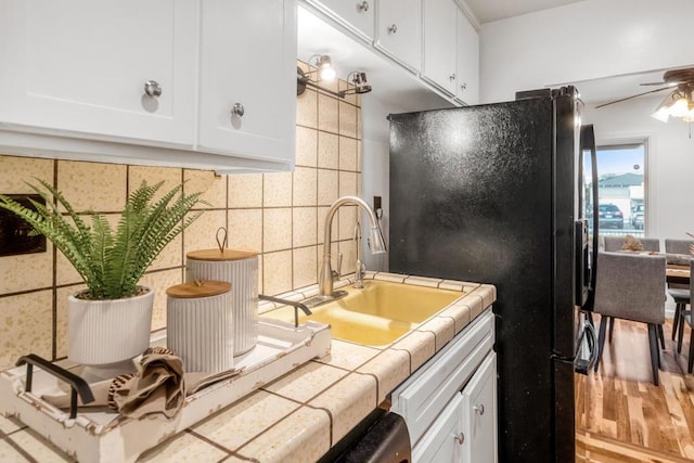 kitchen featuring black refrigerator, white cabinetry, sink, tile counters, and ceiling fan