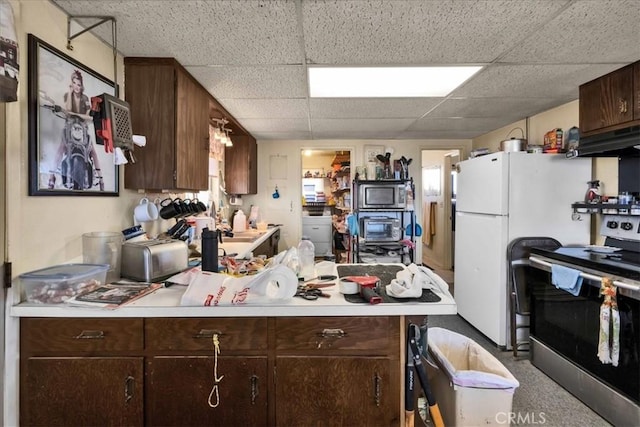 kitchen with a paneled ceiling, appliances with stainless steel finishes, dark brown cabinets, kitchen peninsula, and exhaust hood