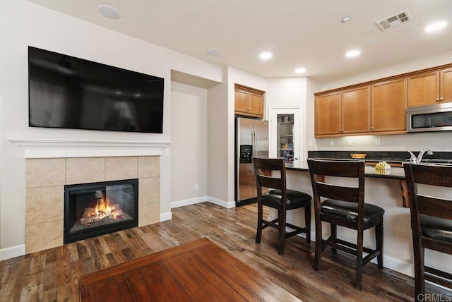 kitchen featuring visible vents, appliances with stainless steel finishes, brown cabinets, dark countertops, and a kitchen bar