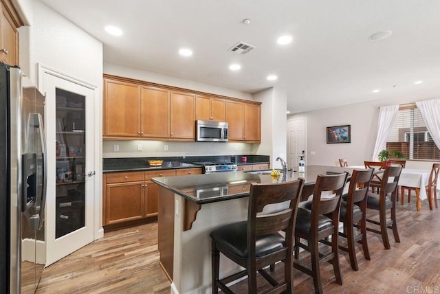 kitchen with visible vents, an island with sink, dark countertops, appliances with stainless steel finishes, and a sink