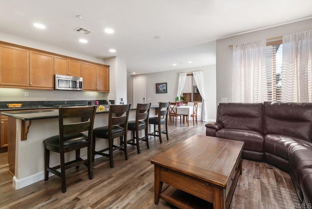 kitchen with visible vents, open floor plan, stainless steel microwave, dark countertops, and a kitchen bar