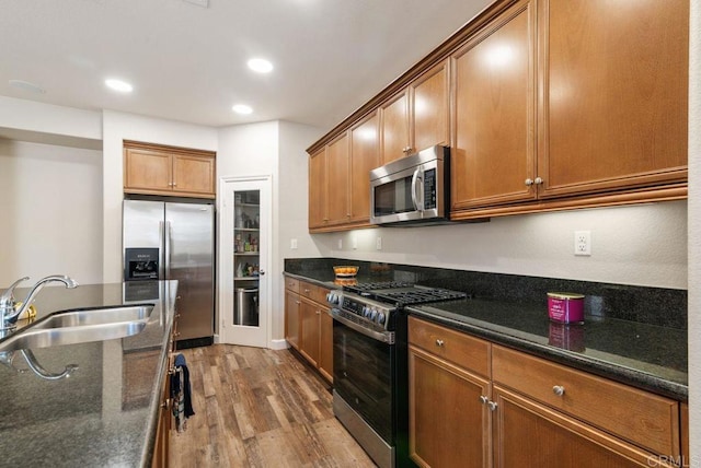 kitchen featuring dark stone counters, brown cabinets, wood finished floors, stainless steel appliances, and a sink