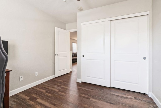 unfurnished bedroom with dark wood-style floors, a closet, and baseboards