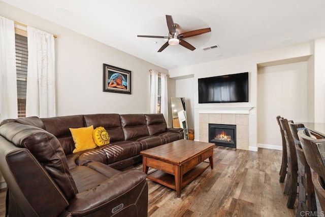 living area featuring ceiling fan, wood finished floors, visible vents, baseboards, and a tiled fireplace