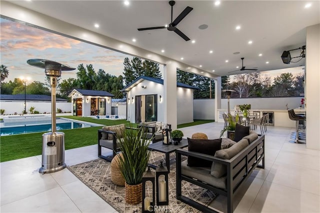 patio terrace at dusk with an outbuilding, ceiling fan, an outdoor living space, and a fenced in pool