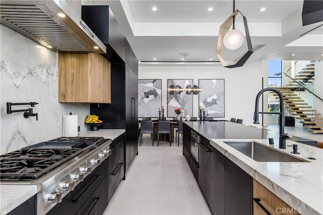 kitchen with sink, stainless steel gas cooktop, light stone counters, pendant lighting, and wall chimney range hood