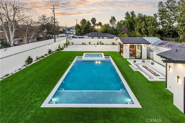 pool at dusk featuring an outbuilding, a yard, and an in ground hot tub