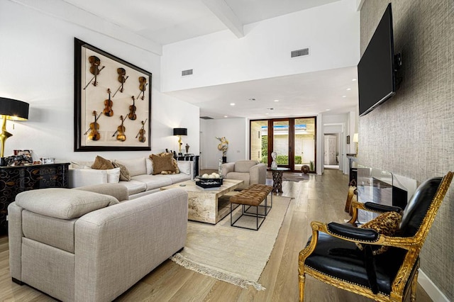 living room featuring a towering ceiling, beam ceiling, and light wood-type flooring