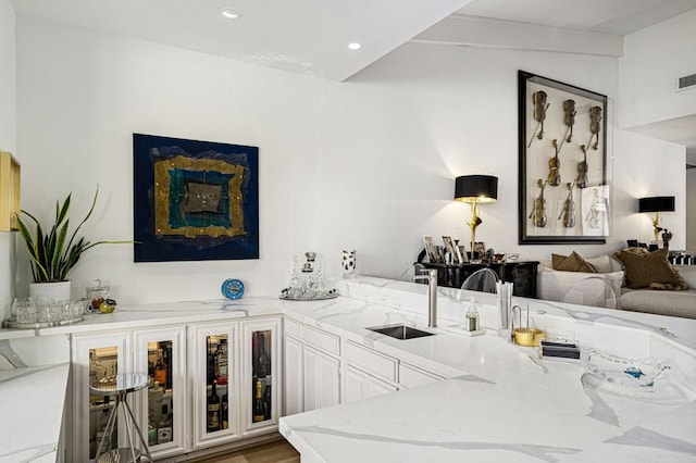 bar featuring sink, hardwood / wood-style flooring, light stone countertops, and white cabinets