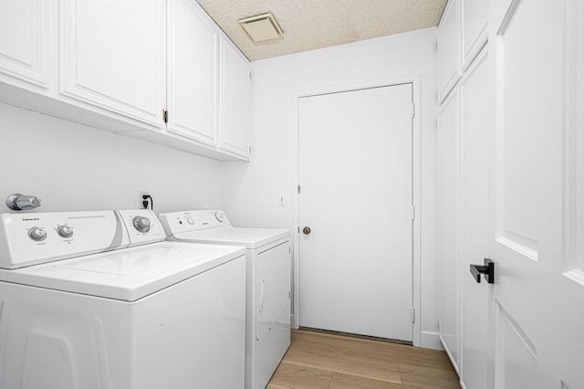 laundry room with cabinets, washing machine and dryer, a textured ceiling, and light hardwood / wood-style floors